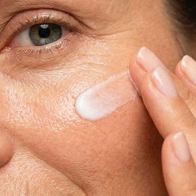 Femme à la peau mature appliquant une crème hydratante sur la joue près de l'œil
