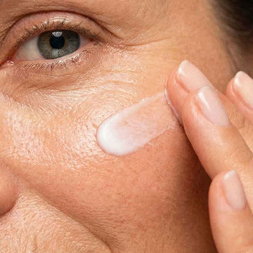 Femme à la peau mature appliquant une crème hydratante sur la joue près de l'œil