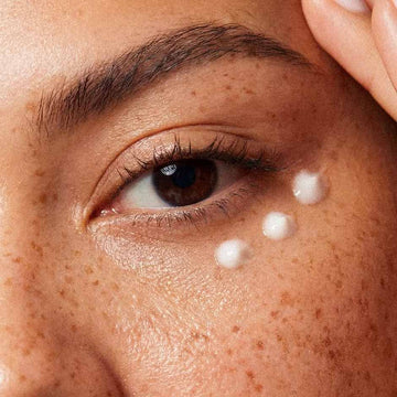 Trois gouttes de crème contour des yeux sous l'œil d'une femme aux taches de rousseur