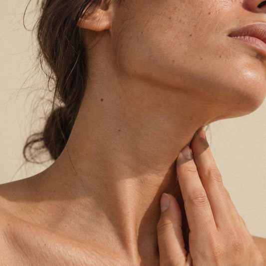 Femme effleurant la base de son cou du bout des doigts, zone de la thyroïde