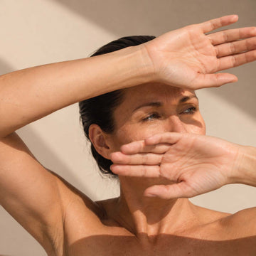 Femme protégeant son visage de ses mains dans la lumière, routine anti-pollution de la peau