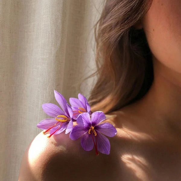 Fleurs de safran aux stigmates rouges posées sur l'épaule d'une femme, actif éclat pour la peau