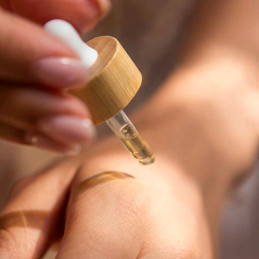 Pipette en bambou déposant une goutte de sérum cosmétique naturel sur le dos d'une main