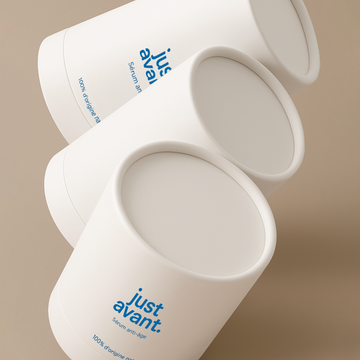 Coffret du sérum visage Lotus bleu Just avant composé de boîtes cylindriques blanches au design épuré, présenté sur fond beige dans une mise en scène graphique.