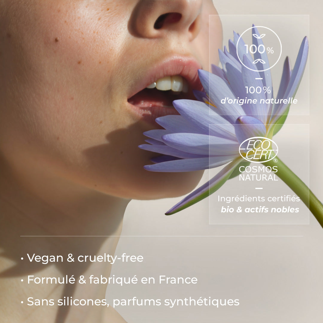 Visage féminin tenant une fleur de lotus bleu, illustrant les engagements du sérum visage Lotus Bleu Just avant. avec labels et mentions de certification affichés sur l’image.