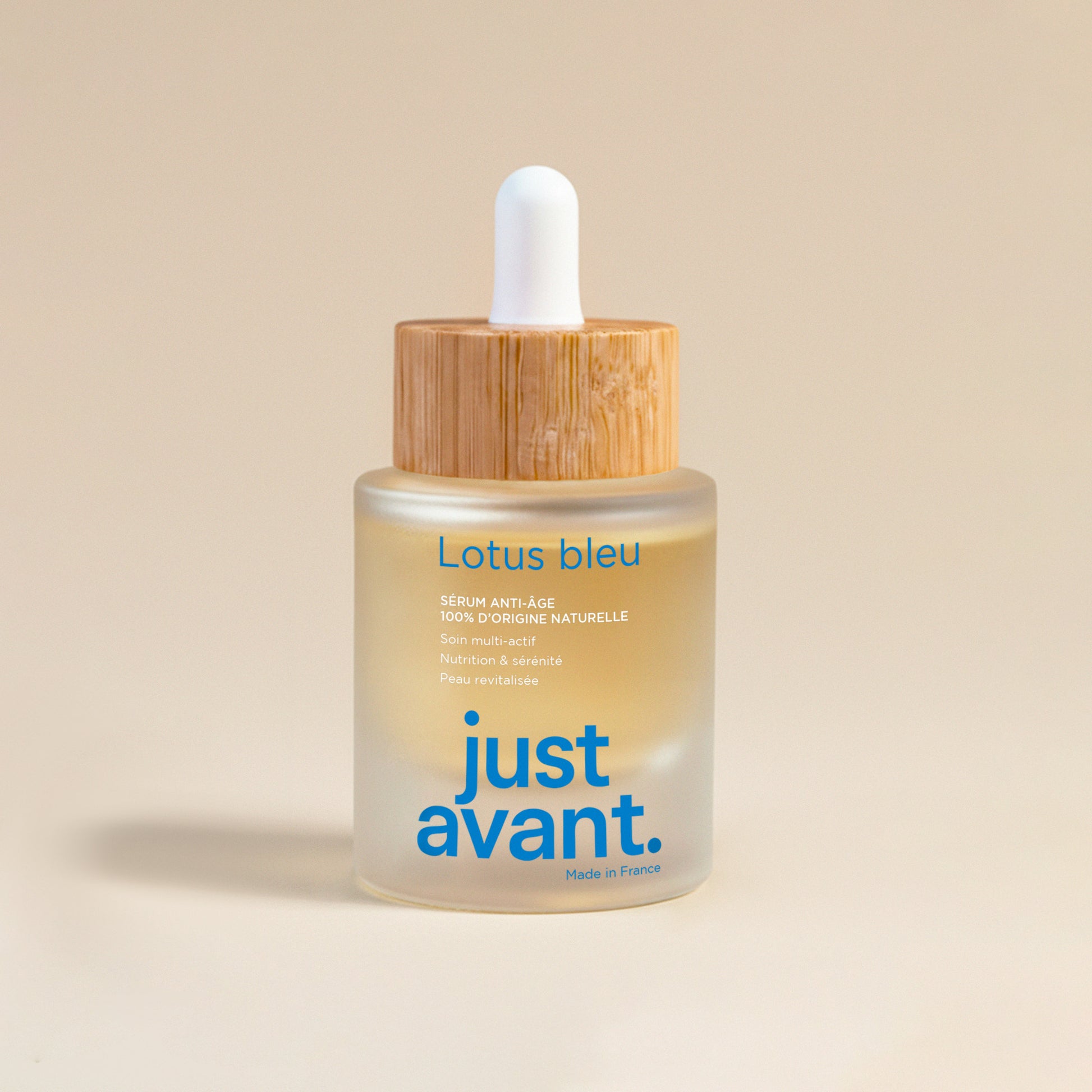 Sérum visage Lotus Bleu Just avant. dans un flacon en verre givré avec pipette blanche et bouchon en bois, soin anti-âge 100% d’origine naturelle présenté sur fond clair.